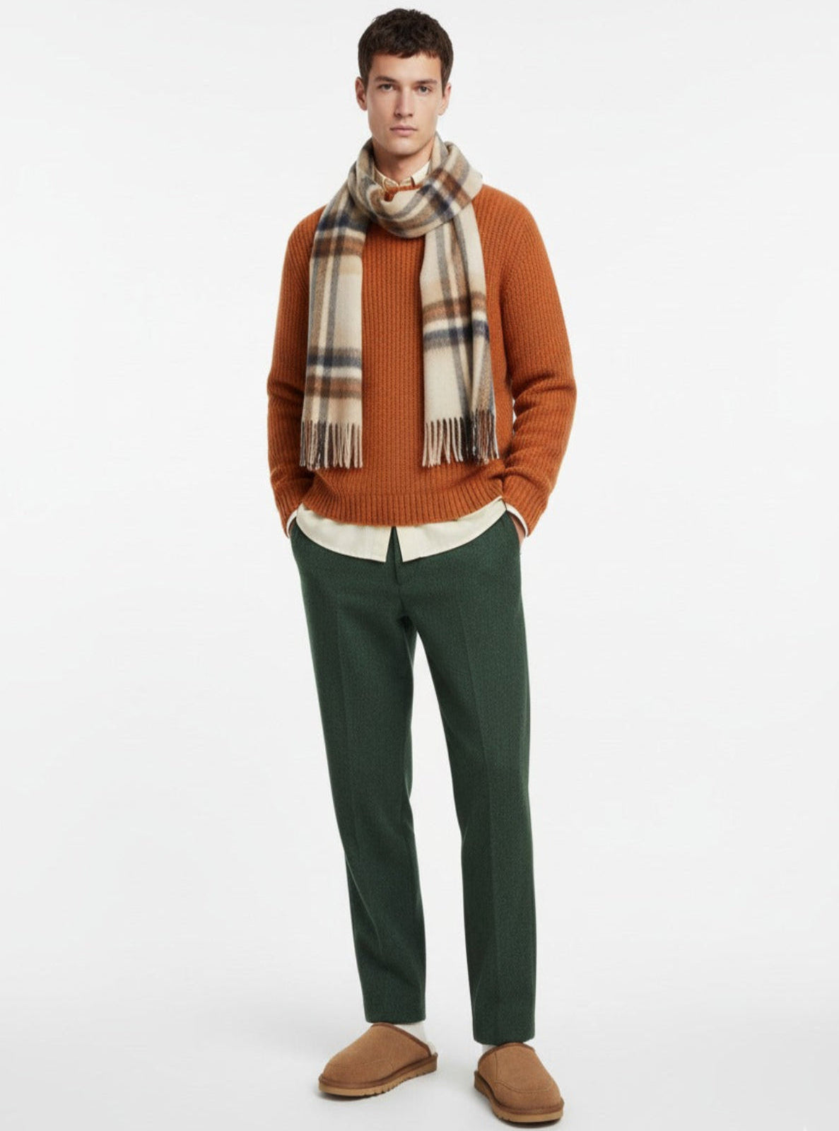 Man wearing a brown sweater, plaid scarf, green pants, and brown shoes on a white background