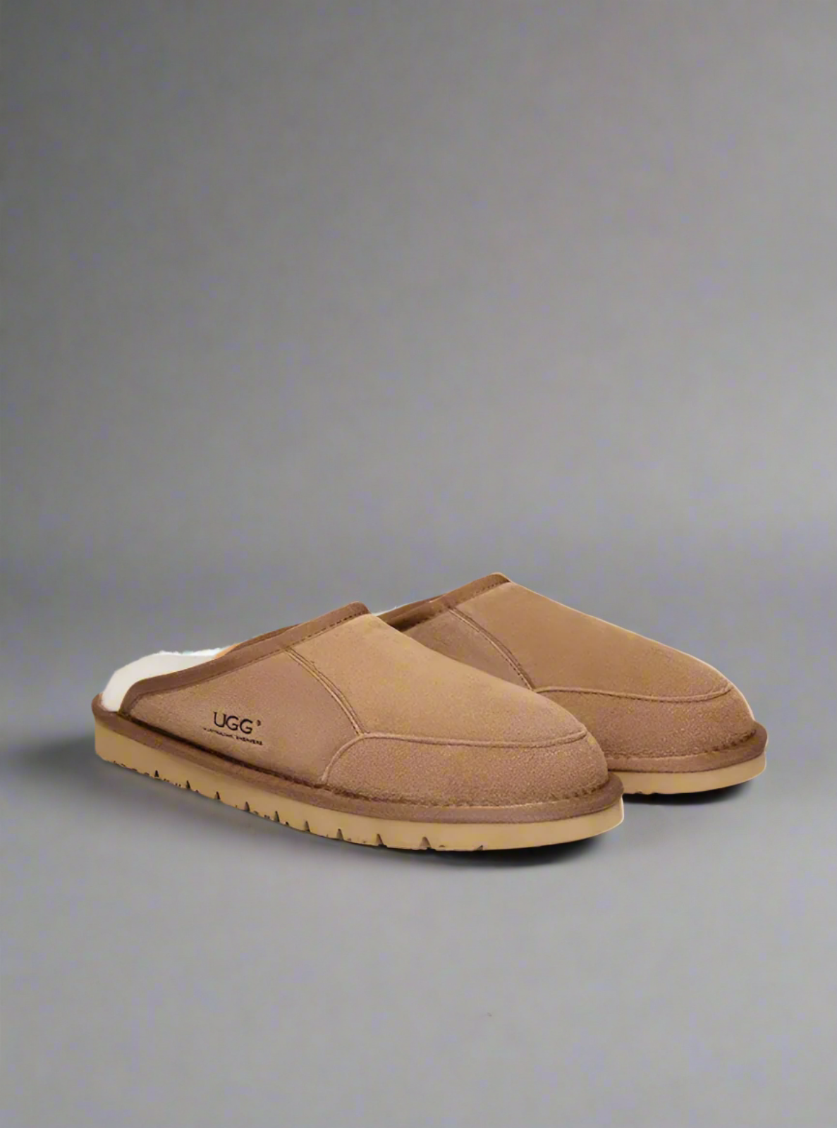 Pair of brown UGG slippers on a gray background