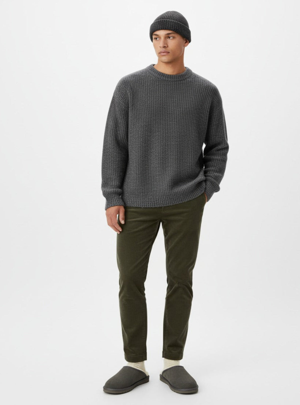 Man wearing a gray sweater, green pants, and gray slippers on a white background