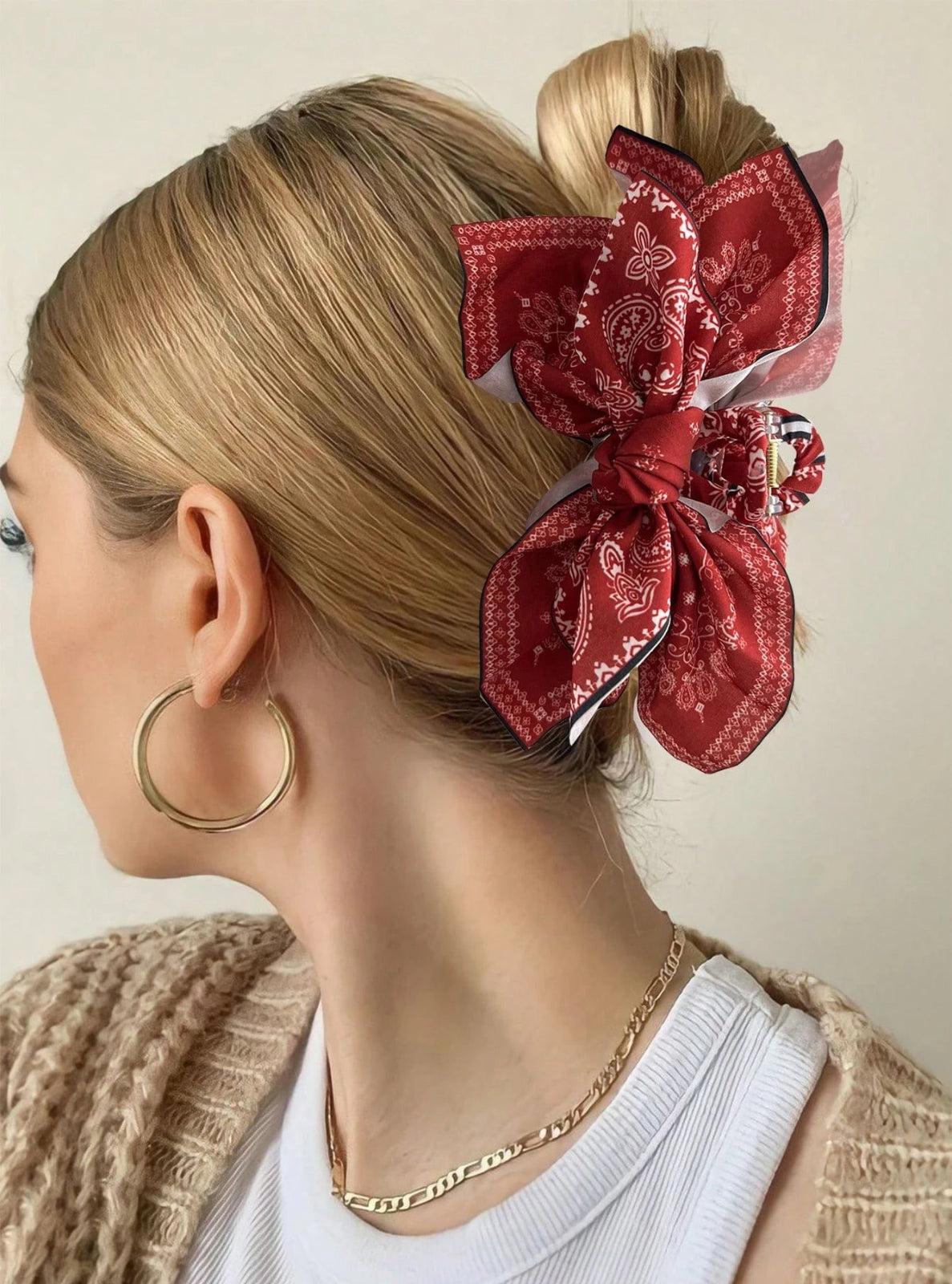 Woman with a red patterned hair bow and gold hoop earrings on a neutral background