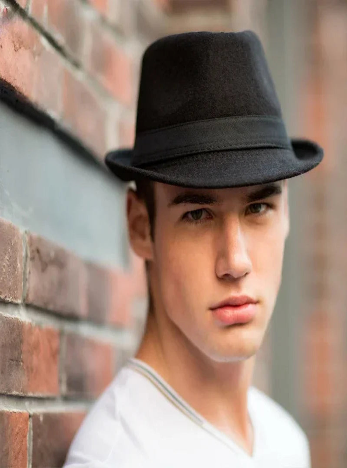 Person wearing a black fedora hat against a brick wall