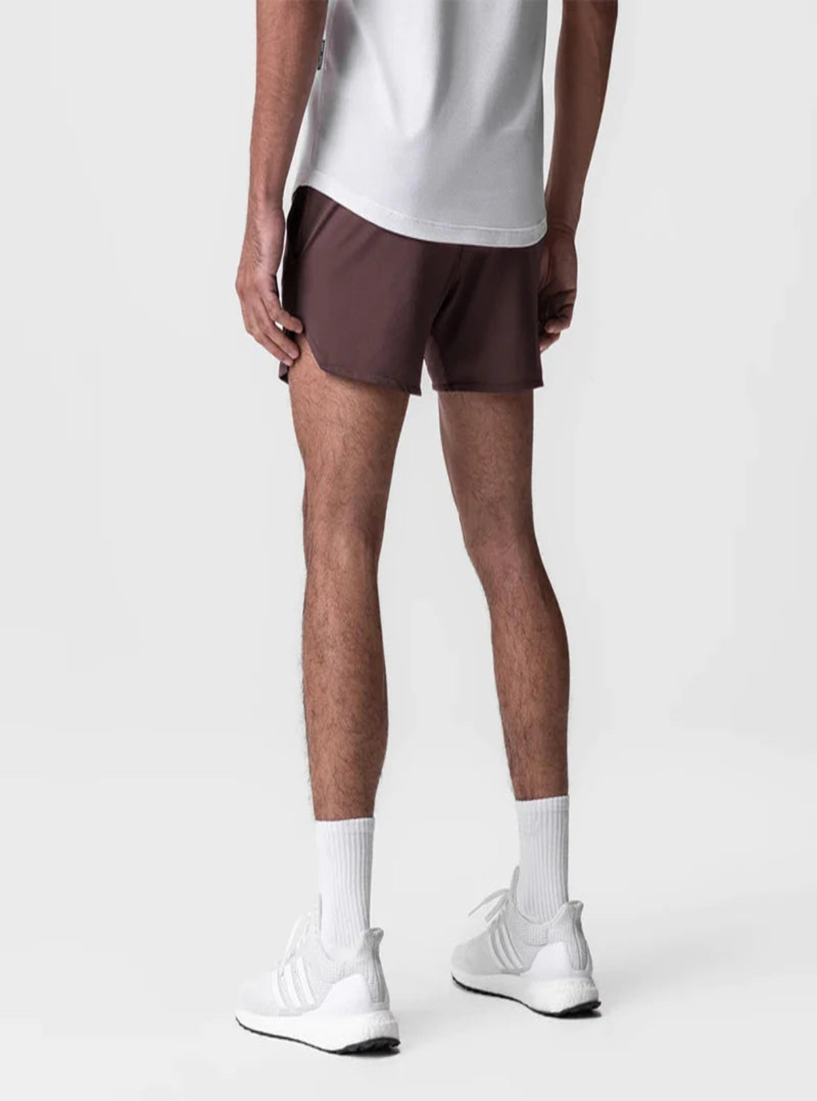 Person wearing brown shorts and white sneakers on a plain background