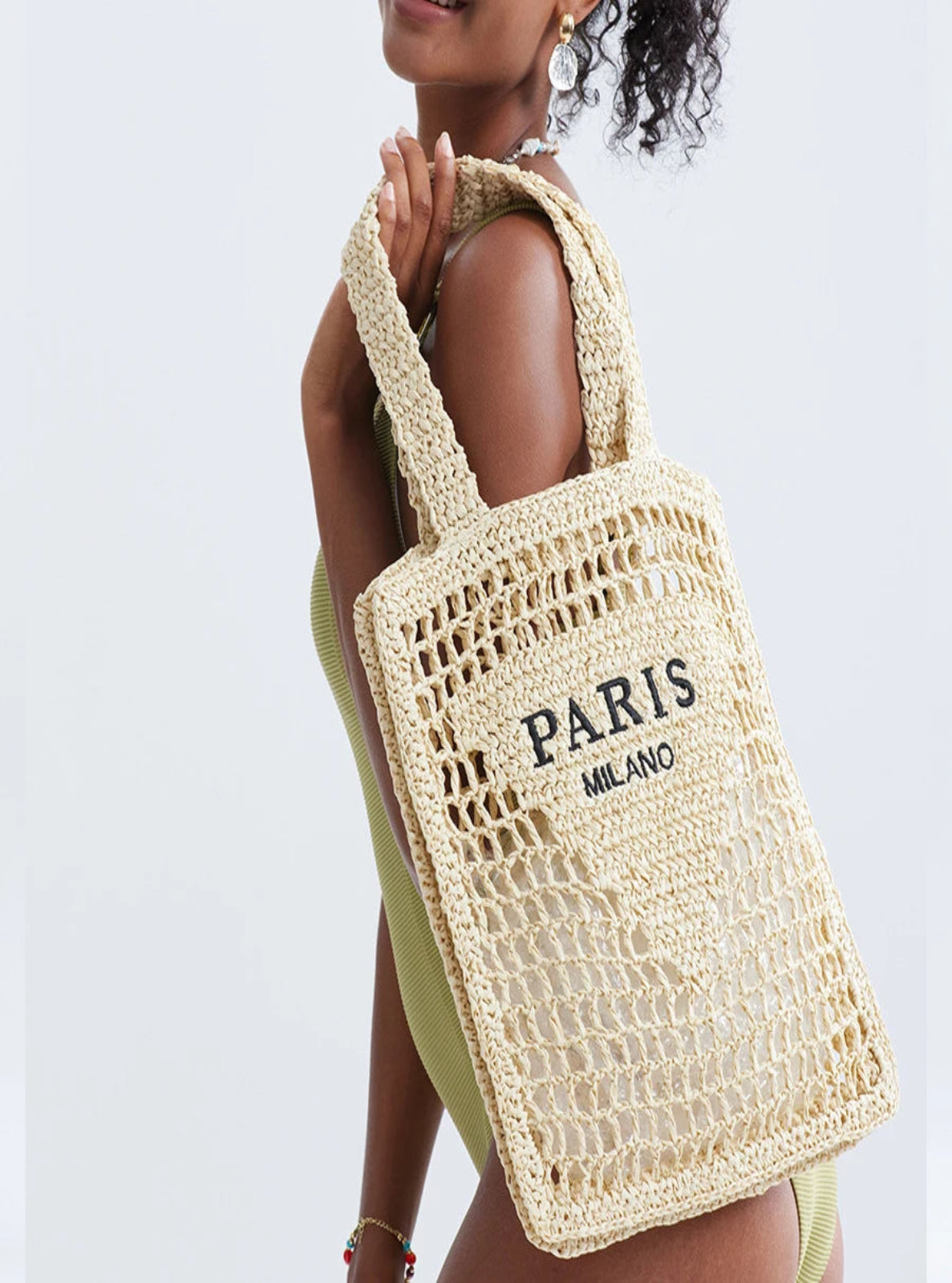 Woman holding a woven bag with 'PARIS MILANO' text against a white background