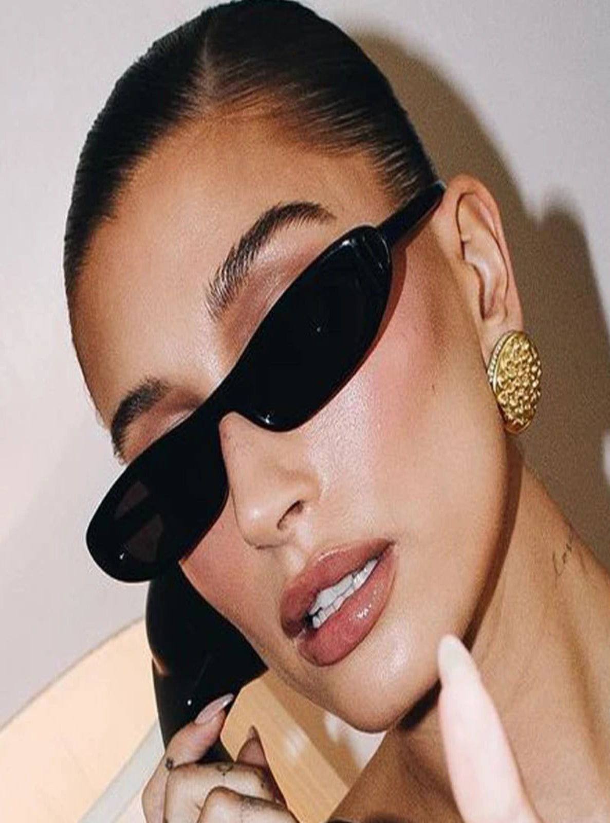 Close-up of a person wearing black sunglasses and a gold earring against a neutral background