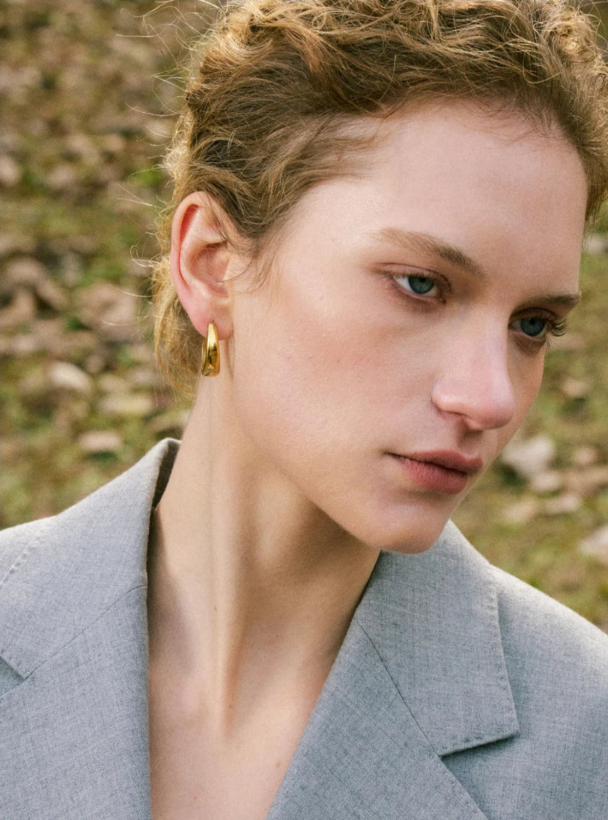 Woman wearing a gold earring with a natural background