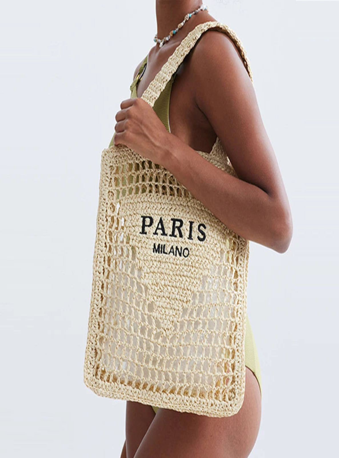 Person holding a woven bag with 'PARIS MILANO' text on a plain background