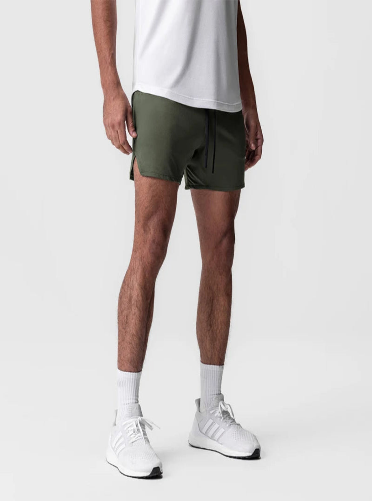 Person wearing green shorts, white shirt, white socks, and white sneakers on a light gray background