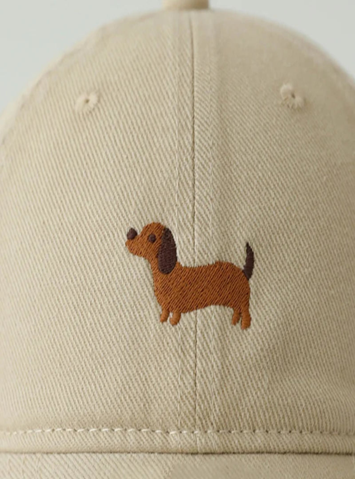 Beige cap with a brown dachshund embroidery on a plain background