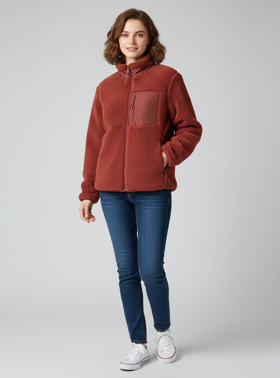 Woman wearing a brown fleece jacket and blue jeans on a gray background