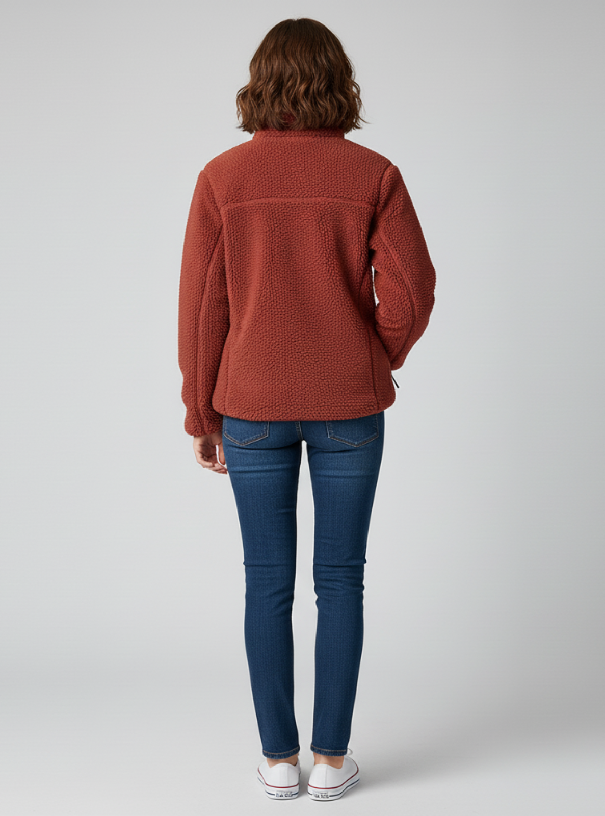 Person wearing a rust-colored sweater and blue jeans on a white background