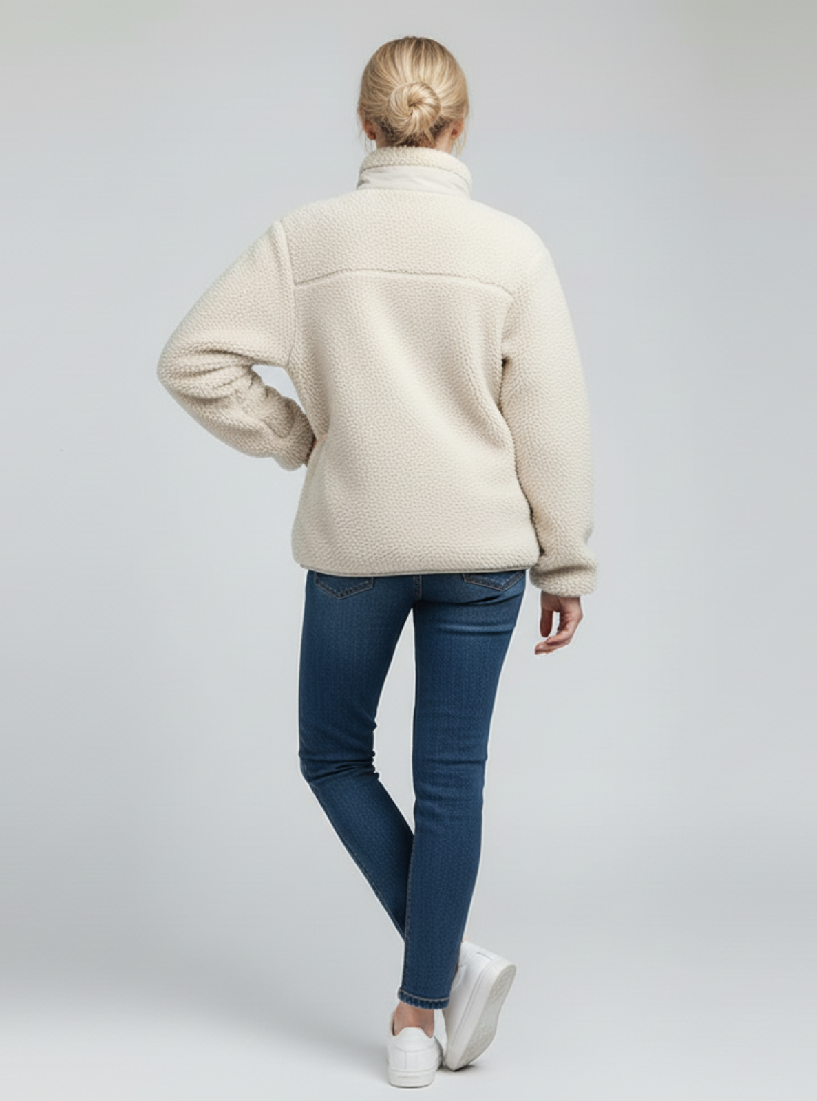 Person wearing a cream jacket and blue jeans on a light gray background