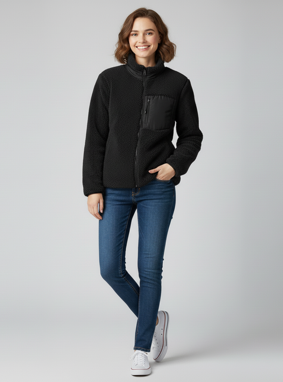 Woman wearing a black jacket and blue jeans on a gray background