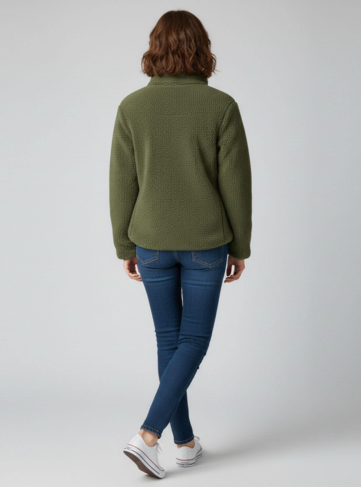 Person wearing a green fleece jacket and blue jeans on a white background