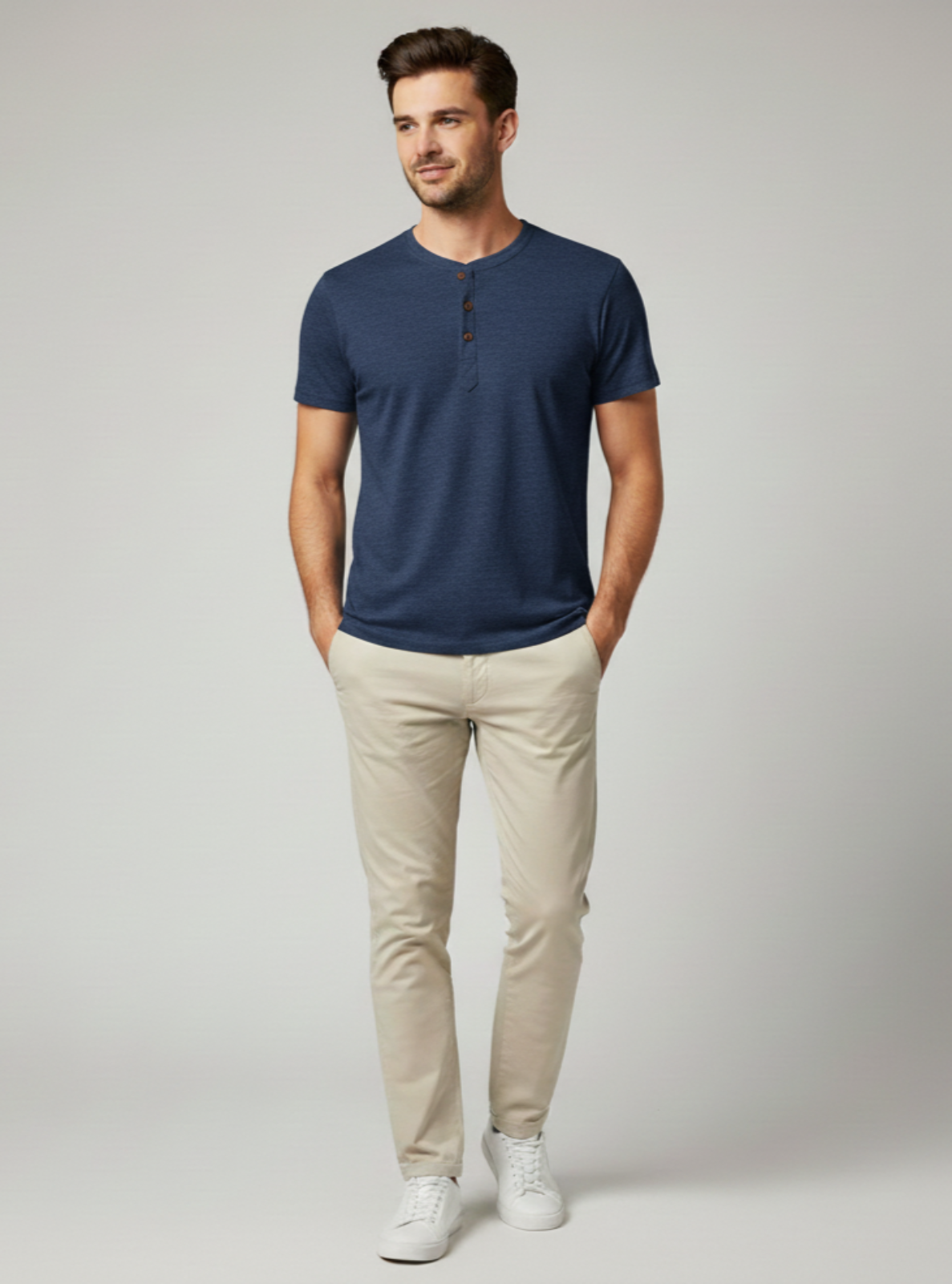 Man wearing a navy blue henley shirt and beige pants on a light gray background