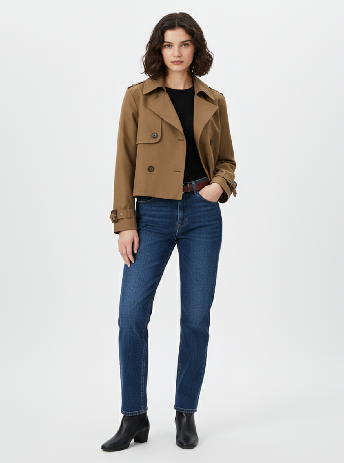 Woman wearing a brown jacket, black top, blue jeans, and black boots on a white background