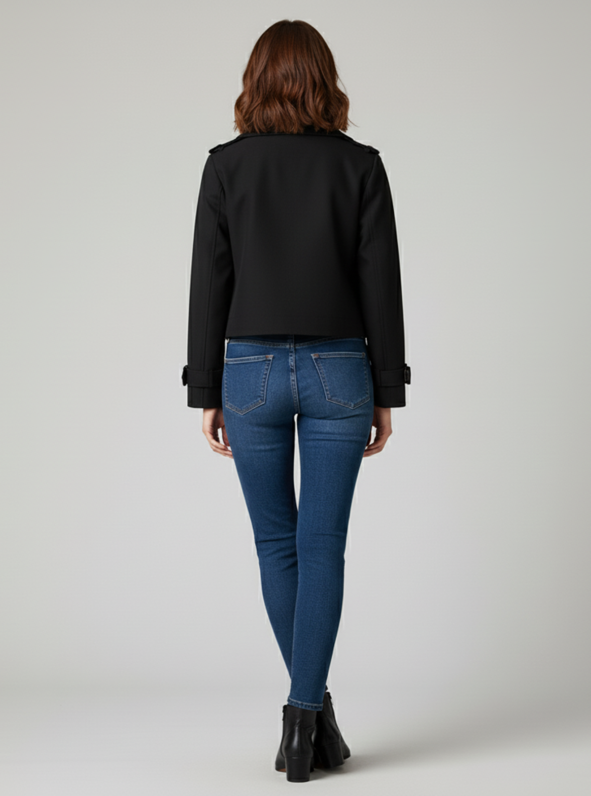 Person wearing a black jacket and blue jeans on a plain background