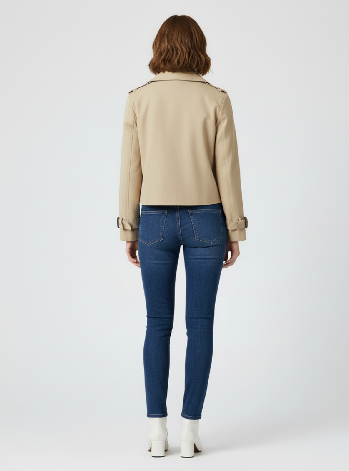 Person wearing a beige jacket and blue jeans on a white background