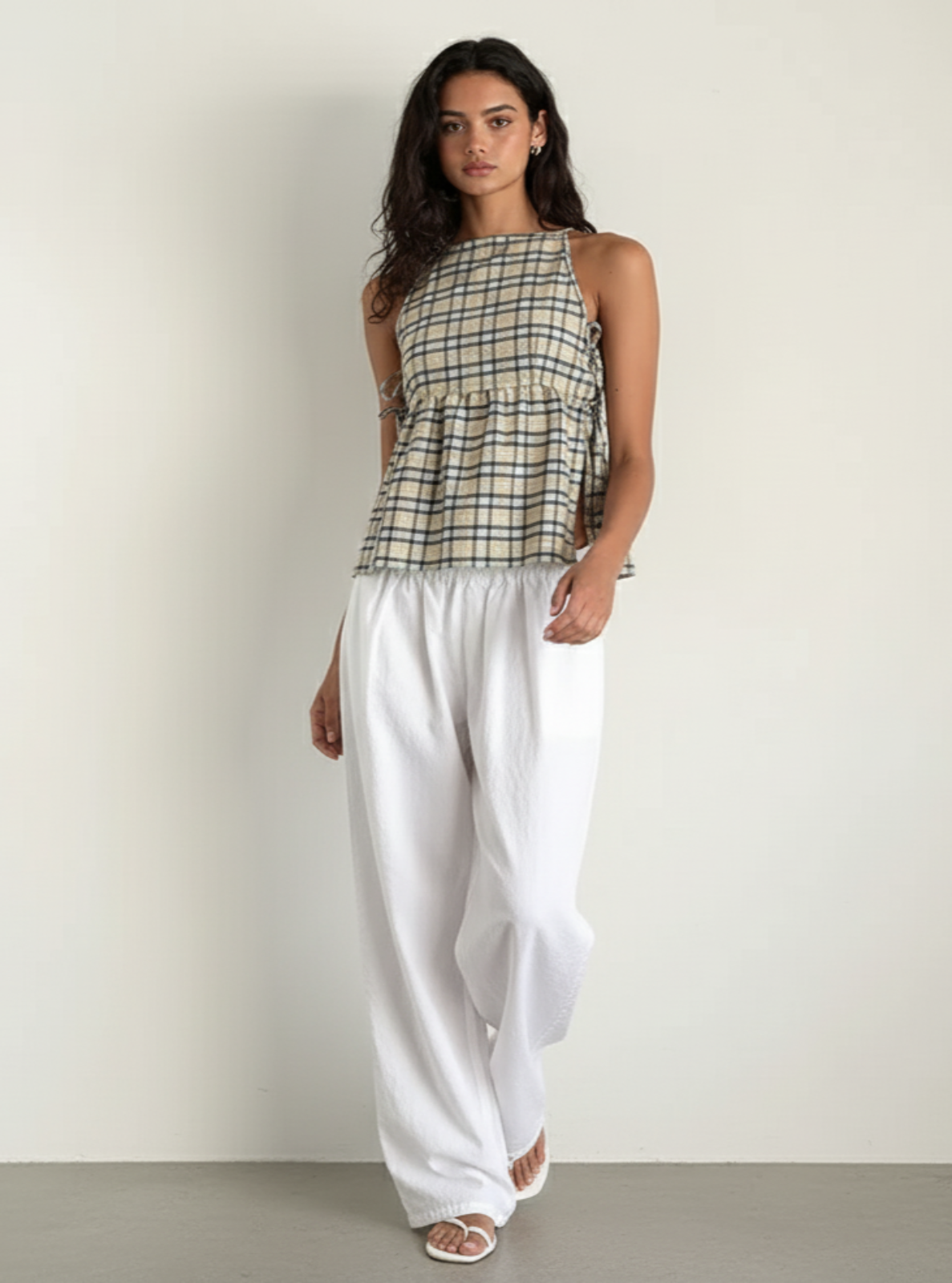 Woman wearing a plaid top and white pants against a plain background