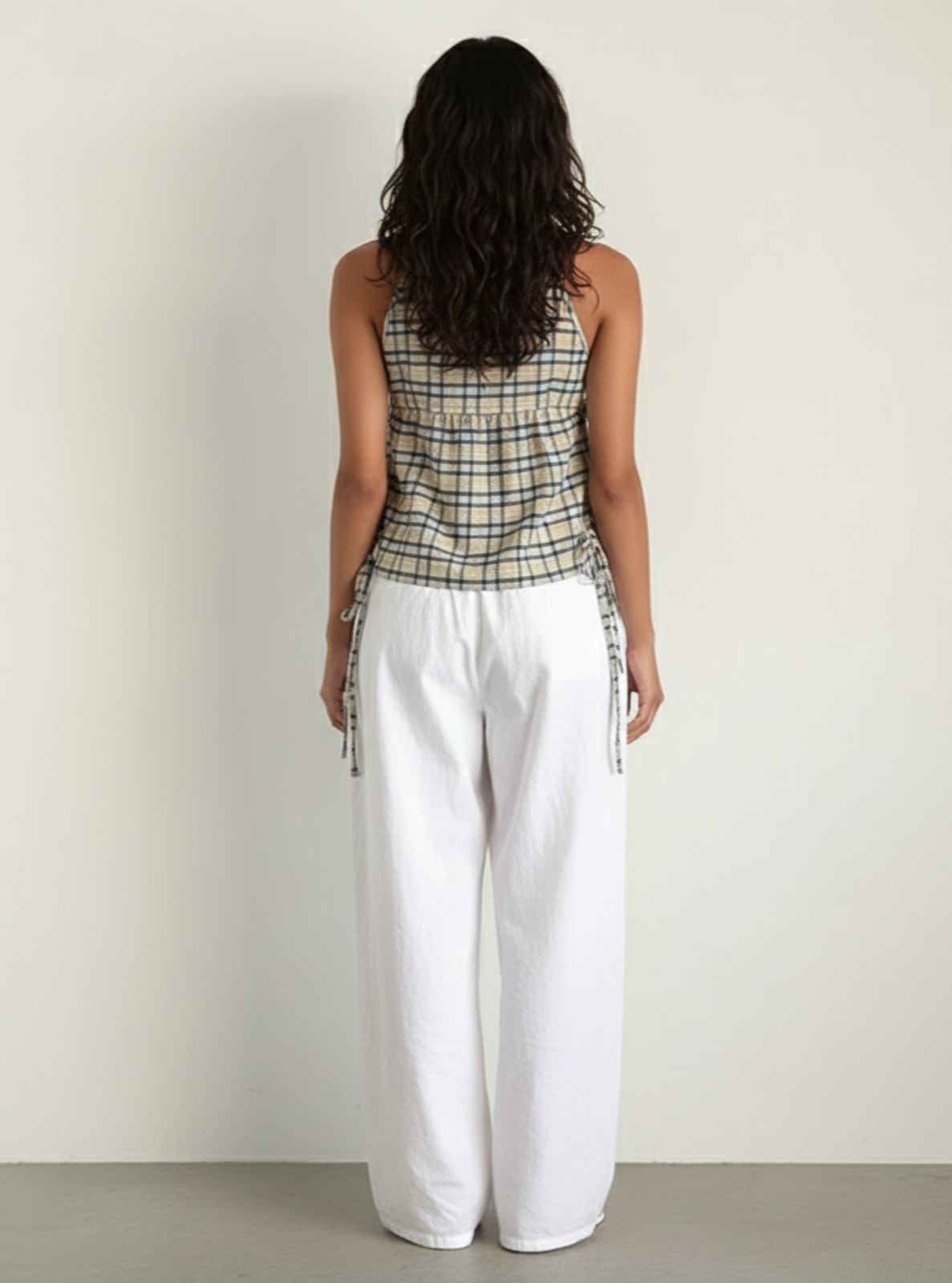 Woman wearing a plaid top and white pants against a plain background
