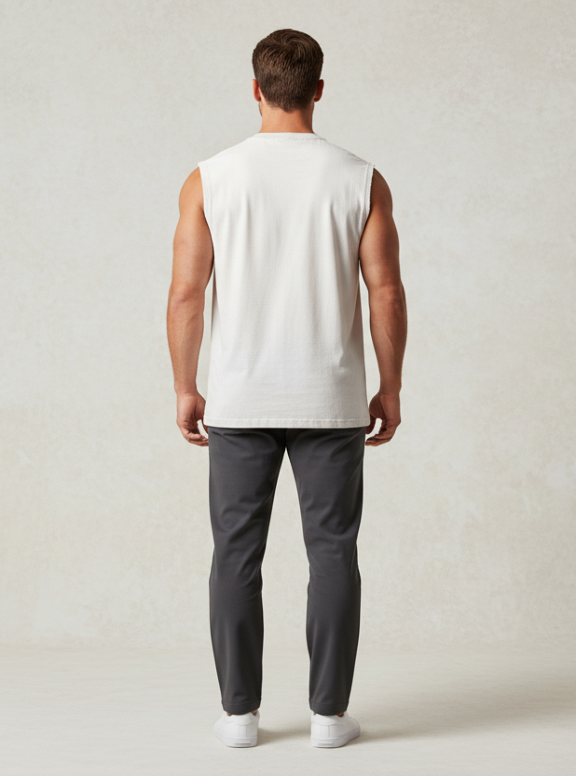 Man wearing a white sleeveless shirt and gray pants against a plain background
