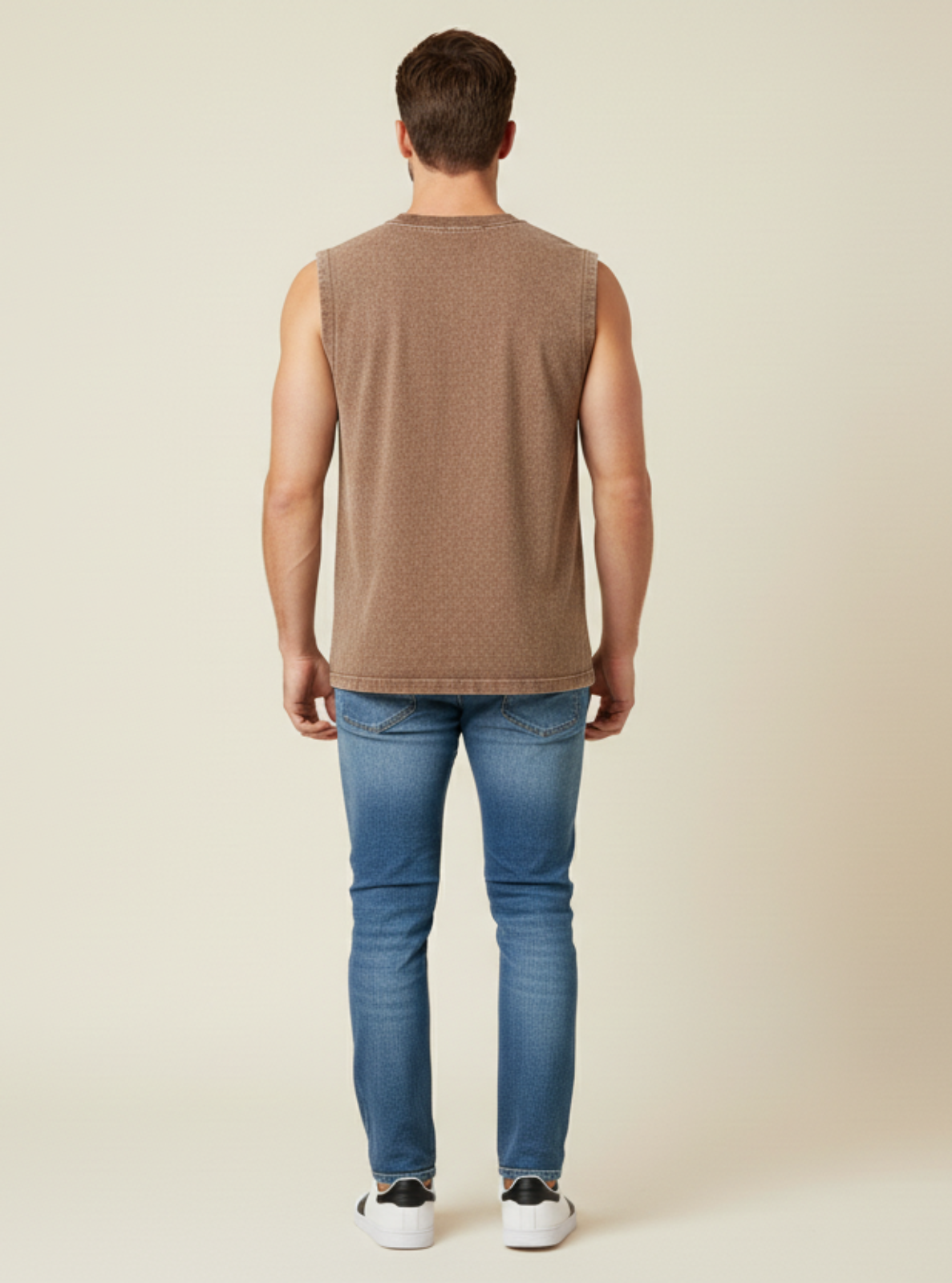 Man wearing a brown sleeveless shirt and blue jeans on a beige background