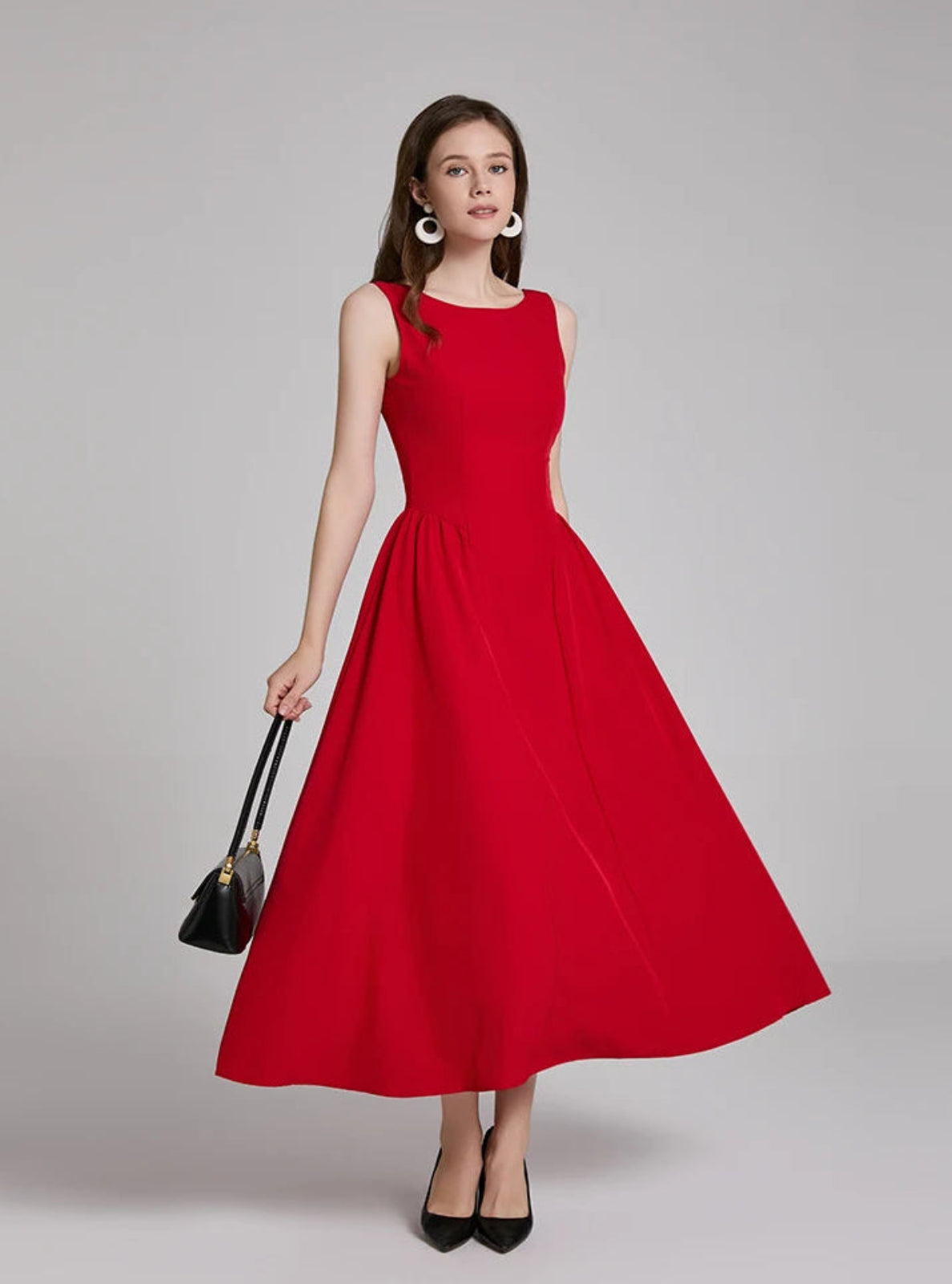 Woman wearing a red dress holding a black handbag on a gray background