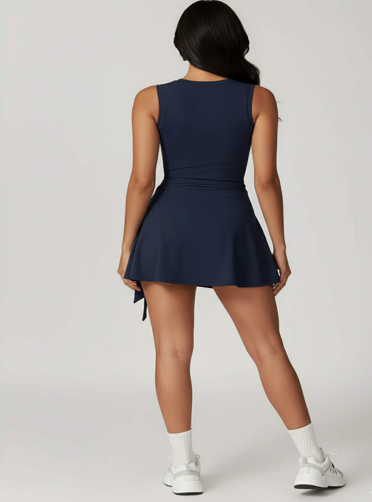 Person wearing a navy blue dress with white sneakers on a light gray background