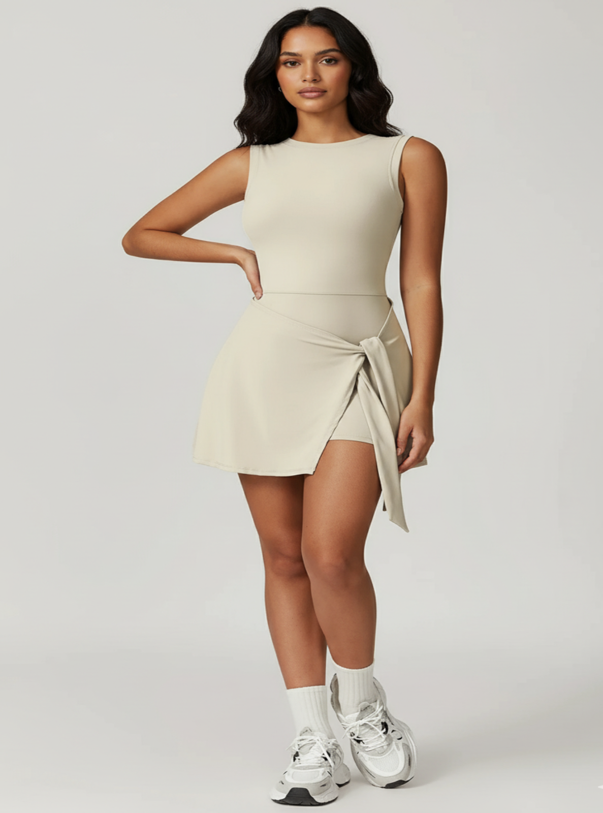 Woman wearing a beige sleeveless dress with a slit on a light gray background