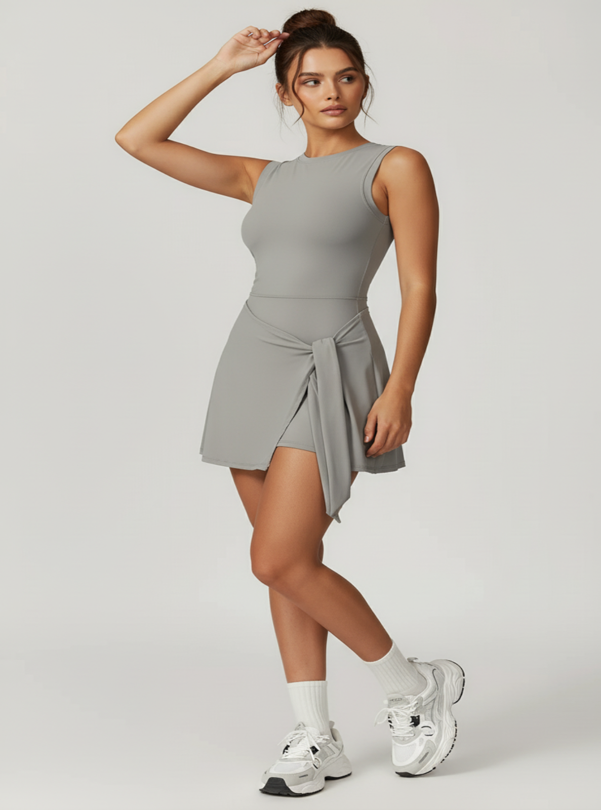 Woman wearing a gray sleeveless dress with a tie detail on a light gray background