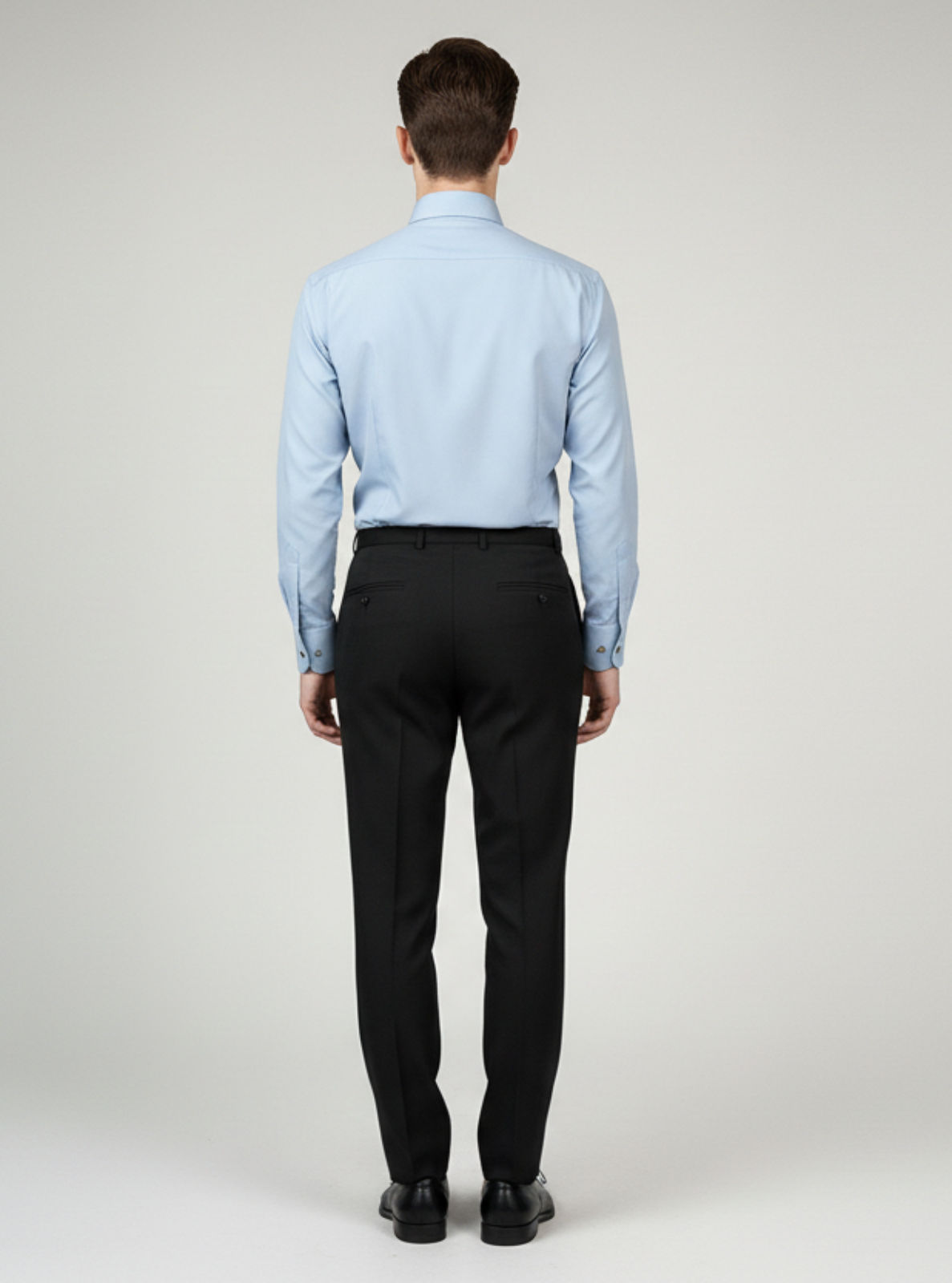 Man wearing a light blue dress shirt and black pants on a white background