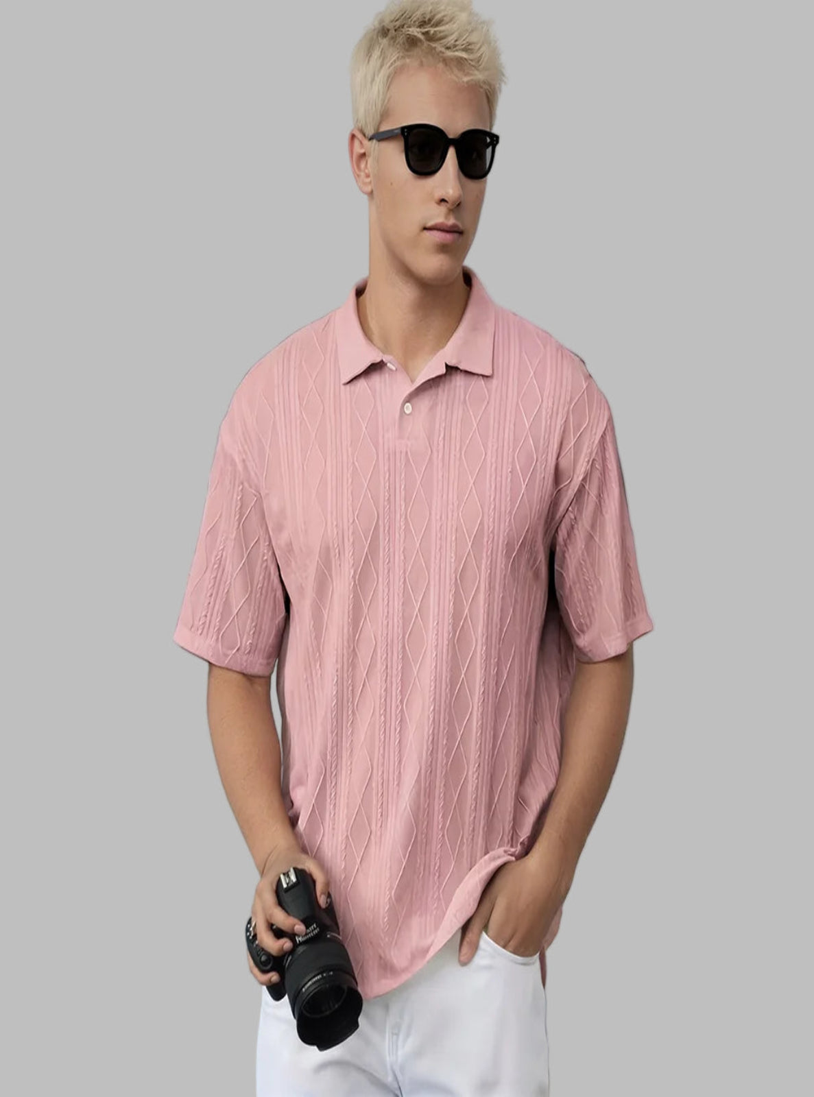 Person wearing a pink patterned shirt and sunglasses, holding a camera against a light blue background