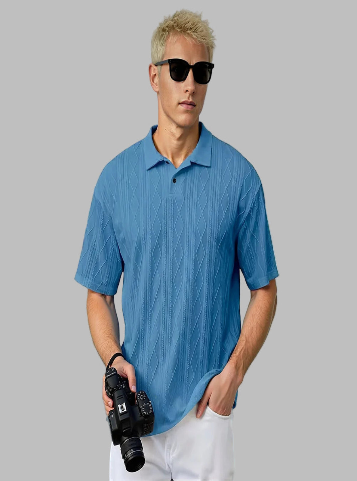 Man wearing a blue textured polo shirt holding a camera indoors.