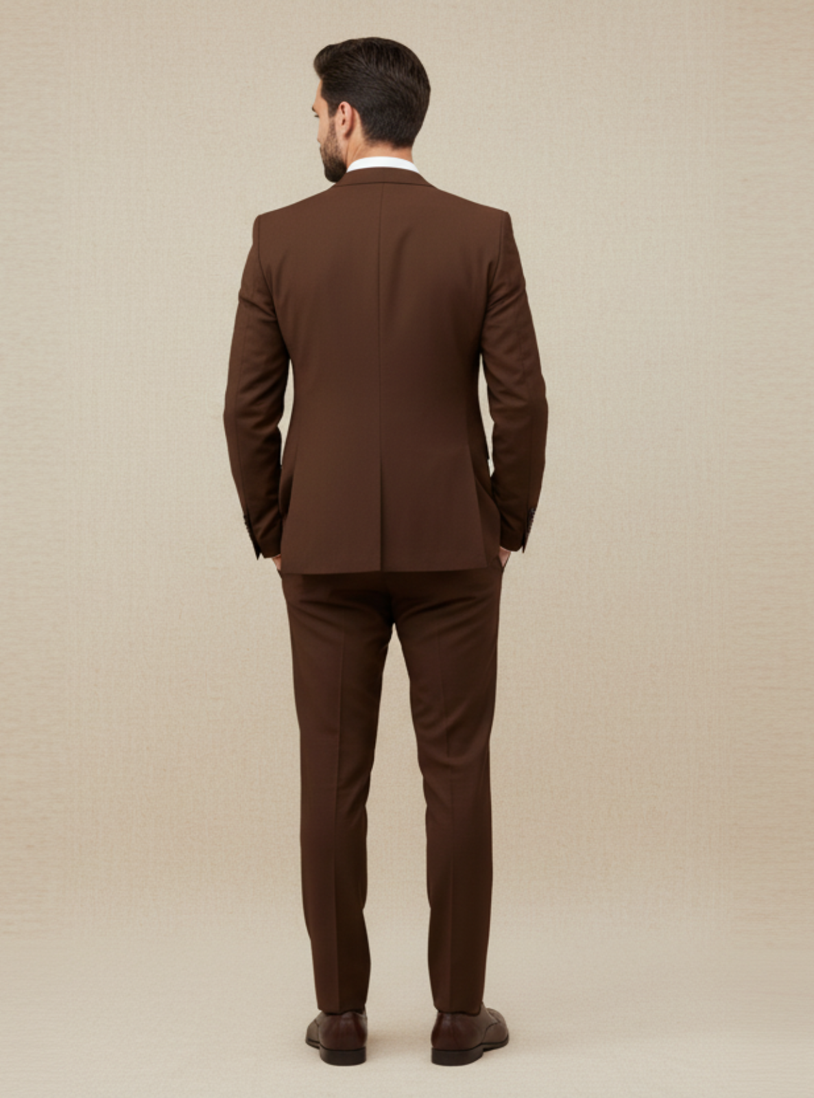 Man wearing a brown suit standing against a beige background