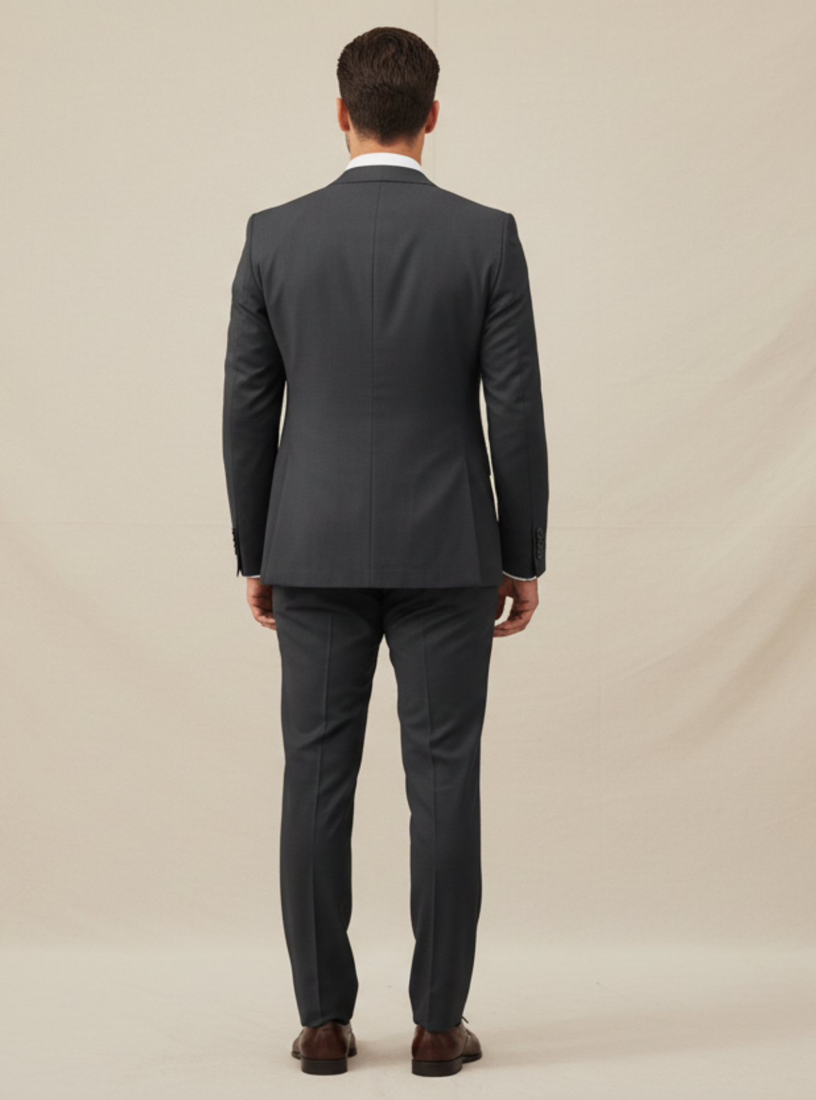 Man wearing a gray suit standing against a beige background