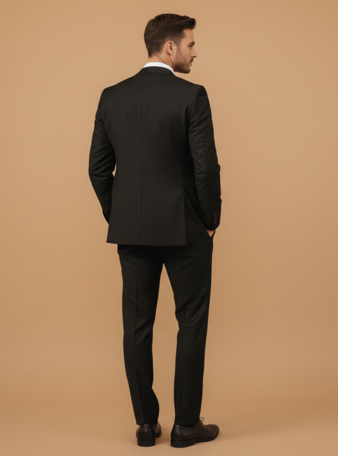 Man wearing a black suit standing against a beige background