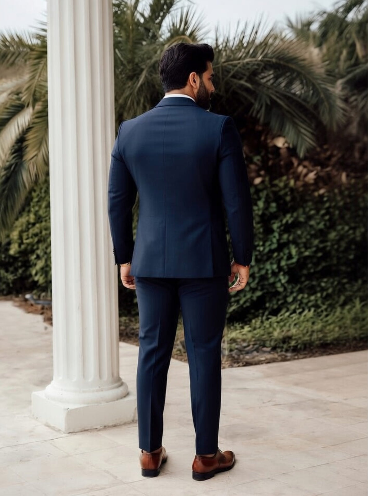 Man in a navy suit standing next to a white column with palm trees in the background
