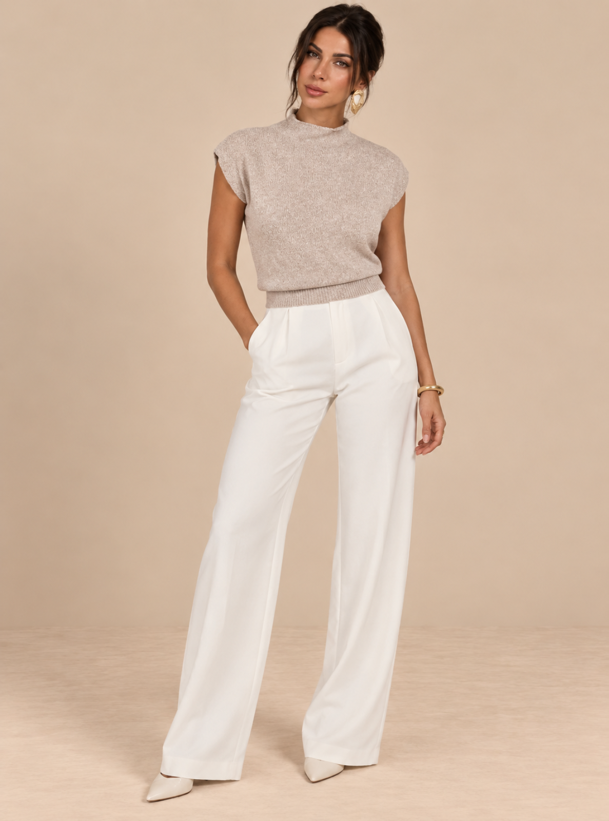 A woman modeling a light beige short-sleeve knit mock-neck top paired with high-waisted white wide-leg trousers, standing against a solid beige studio backdrop.