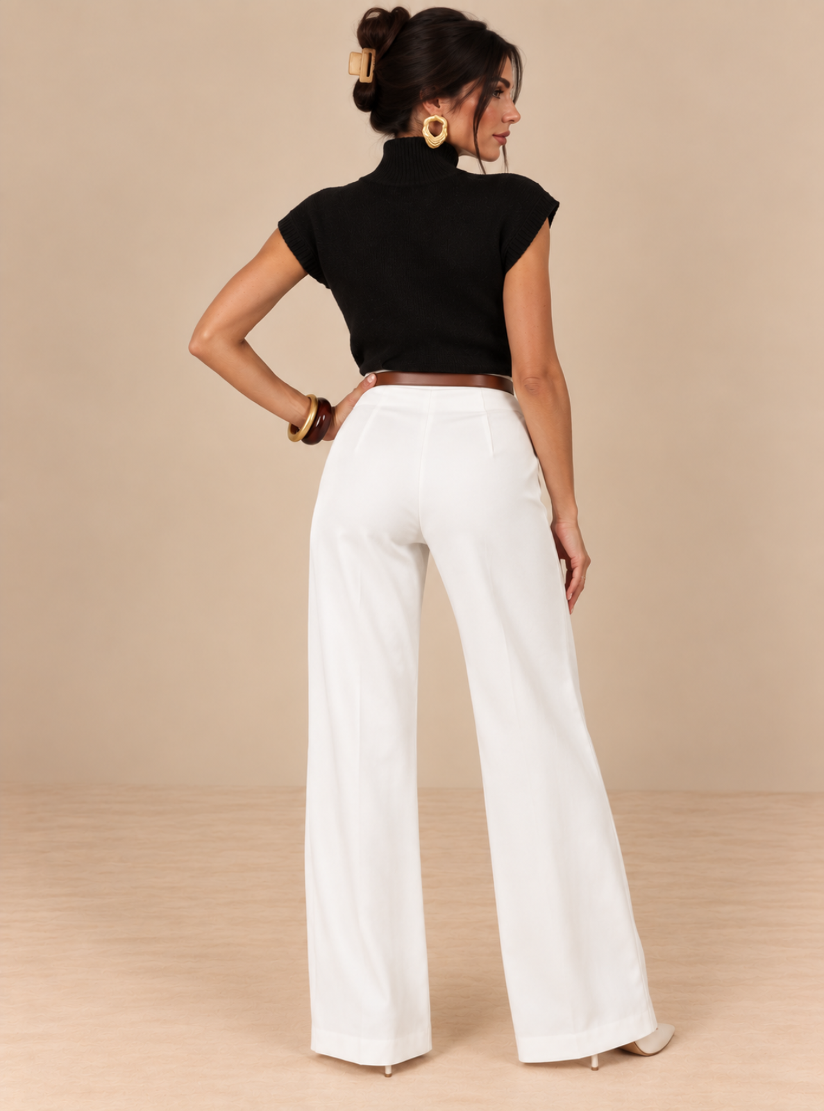 A woman shown from the back wearing a black short-sleeve mock-neck top and white wide-leg pants, standing against a plain beige studio backdrop.