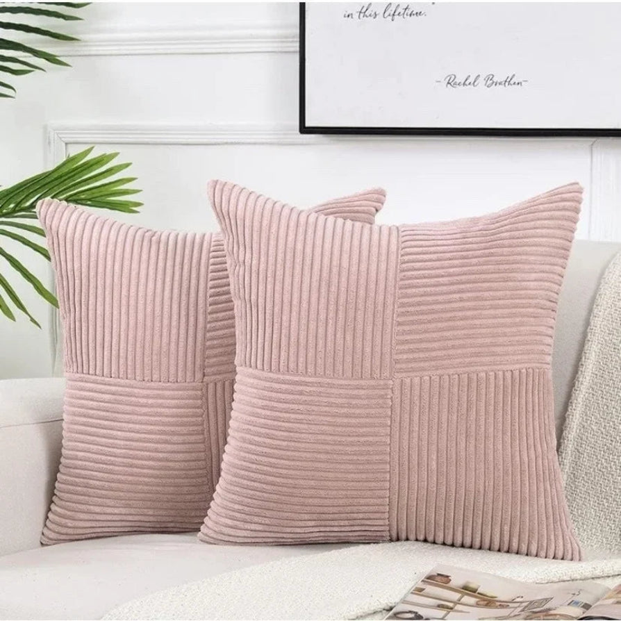 Two pink textured pillows on a white couch with a plant and framed picture in the background.