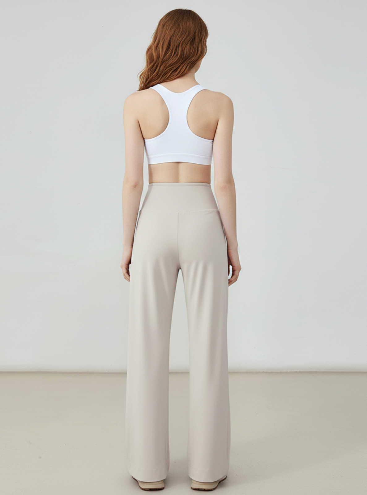 Woman wearing a white sports bra and beige wide-leg pants on a plain background