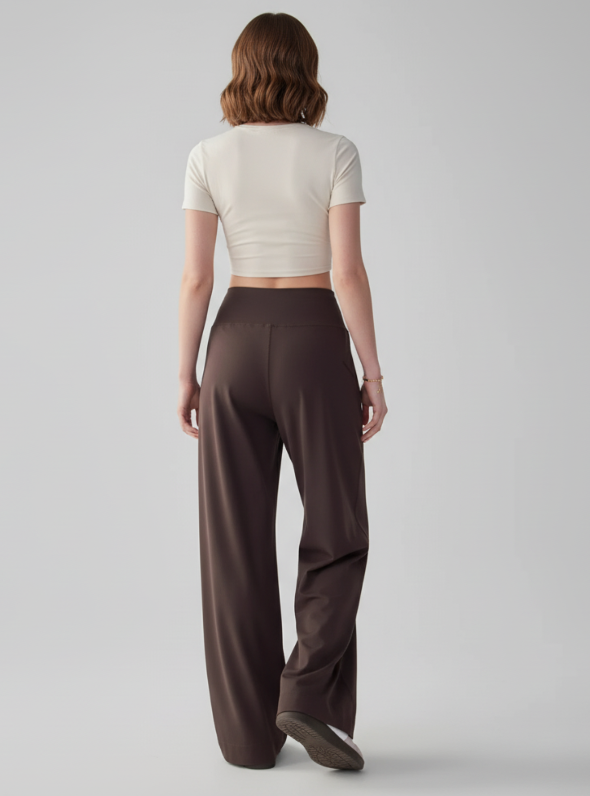 Woman wearing a white crop top and brown wide-leg pants on a gray background
