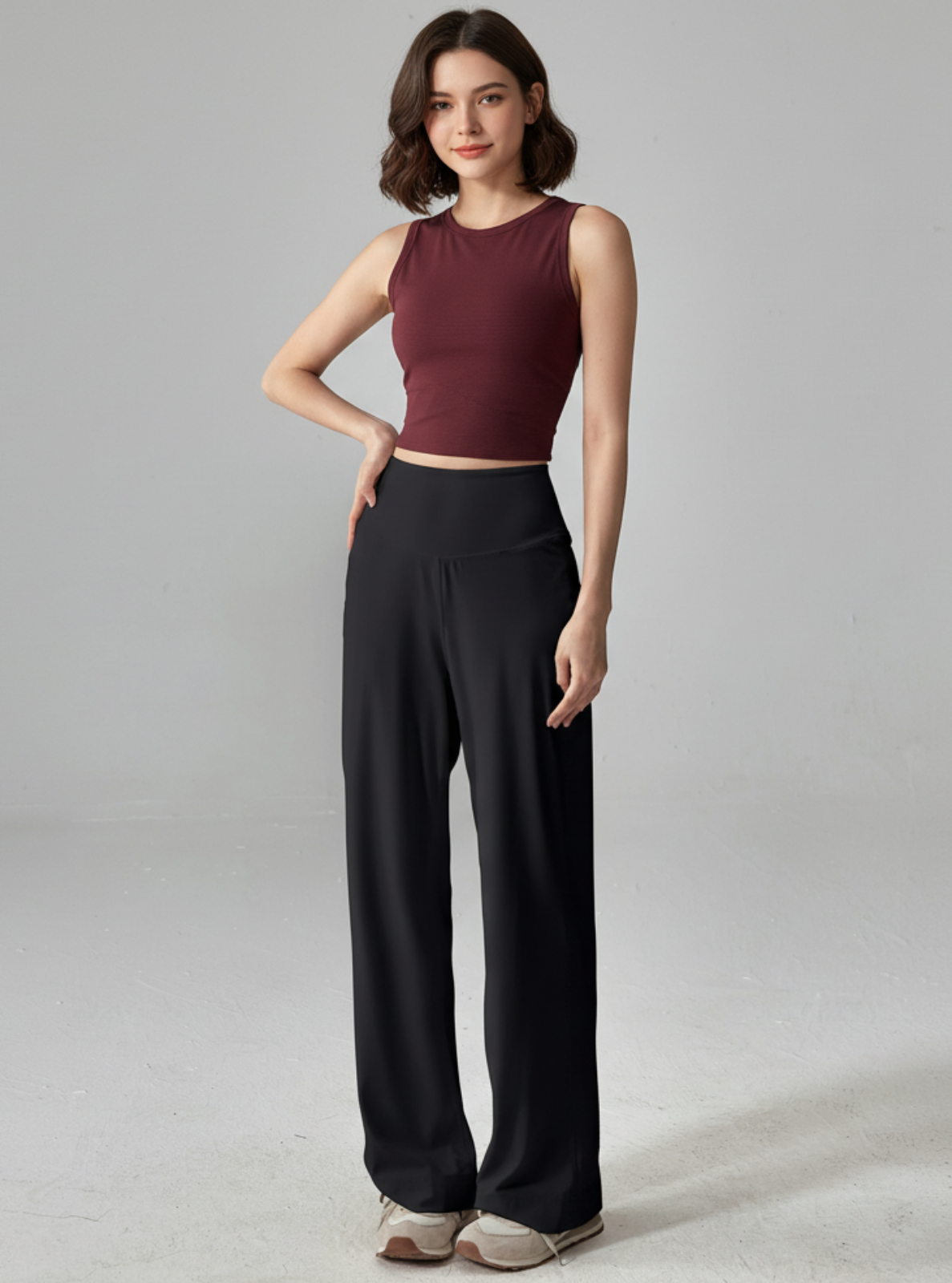 Woman wearing a burgundy sleeveless top and black high-waisted pants on a gray background