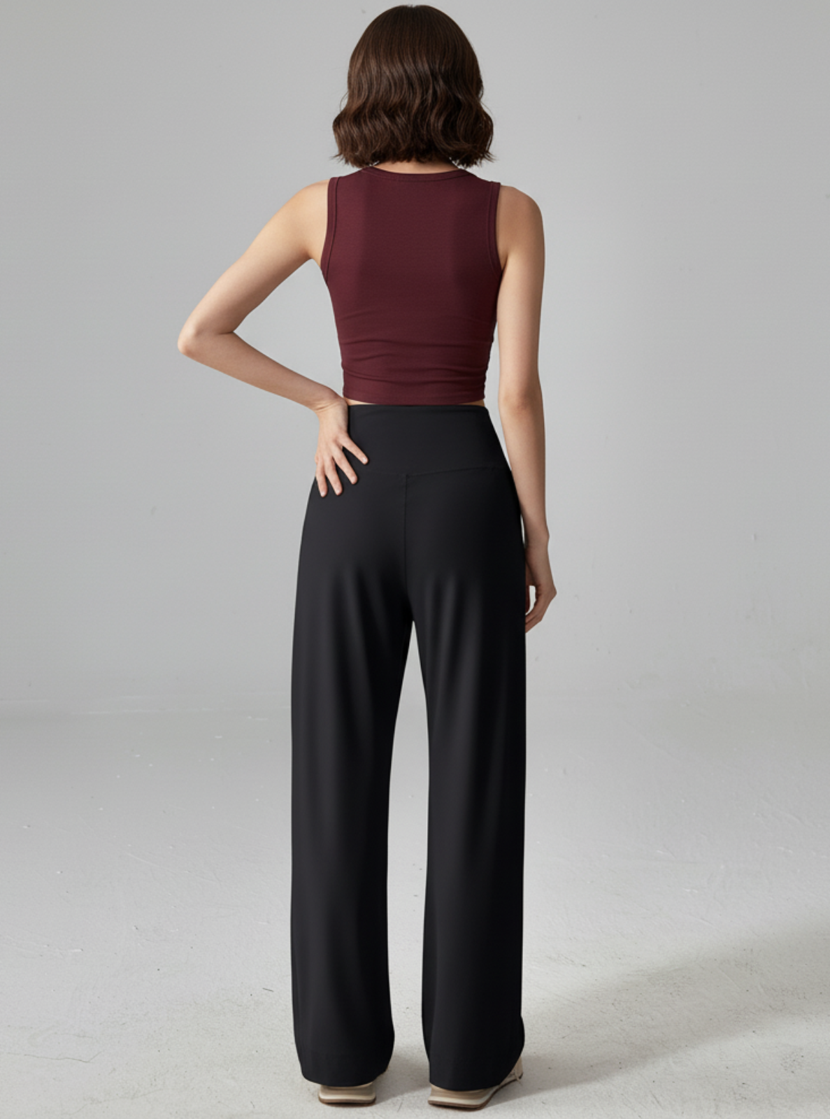 Woman wearing a burgundy sleeveless top and black wide-leg pants on a gray background