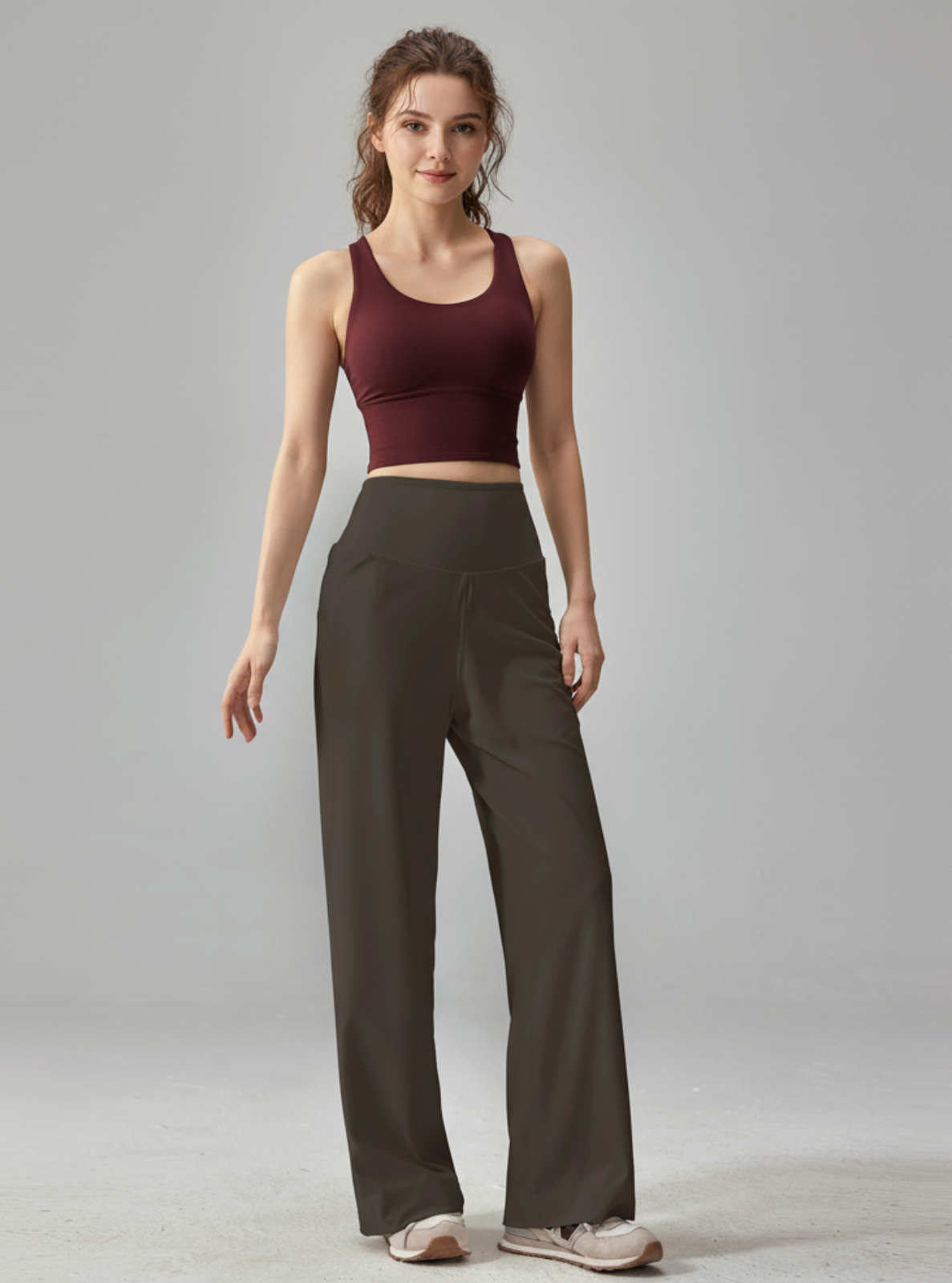 Woman wearing a burgundy sports bra and dark pants on a gray background