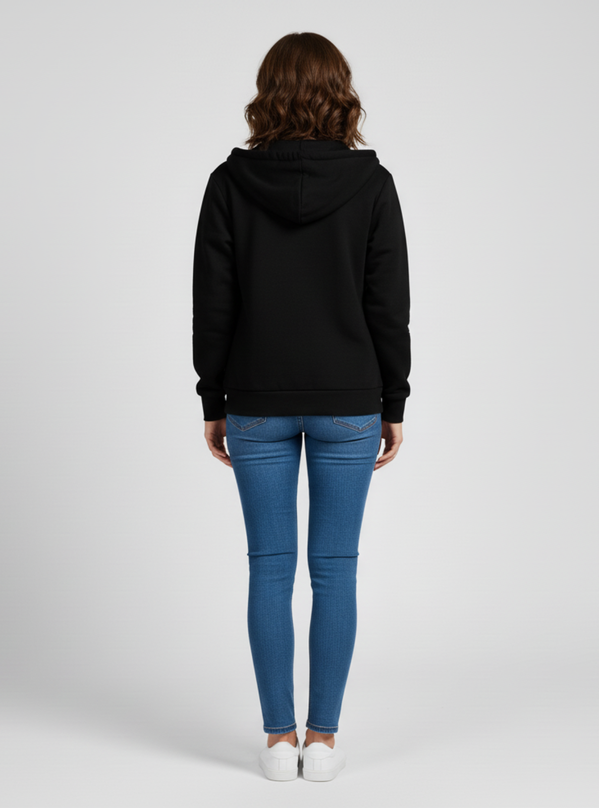 Person wearing a black hoodie and blue jeans on a white background