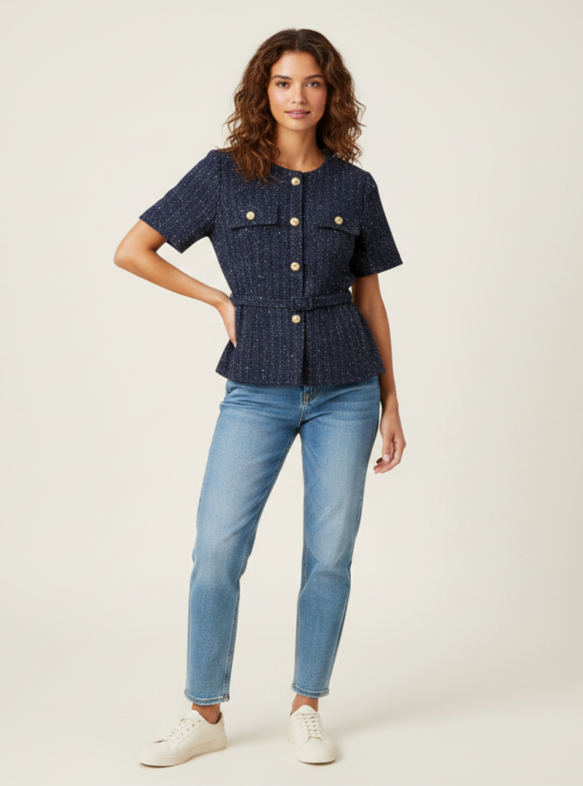 Woman wearing a navy blue top with gold buttons and light blue jeans on a white background