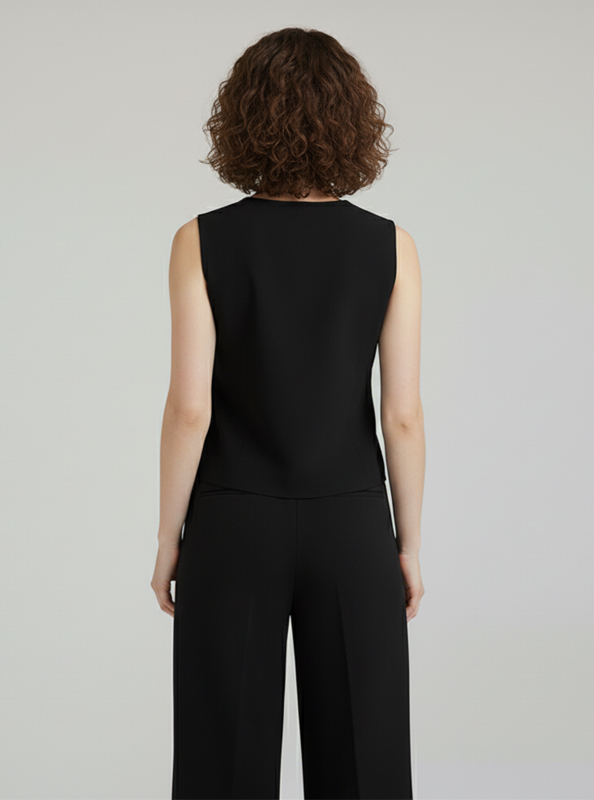 Person wearing a black sleeveless top and pants on a gray background