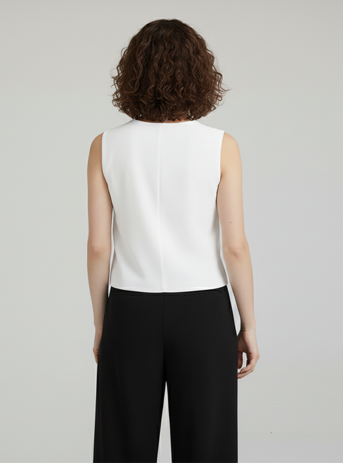 Person wearing a white sleeveless top and black pants on a plain background