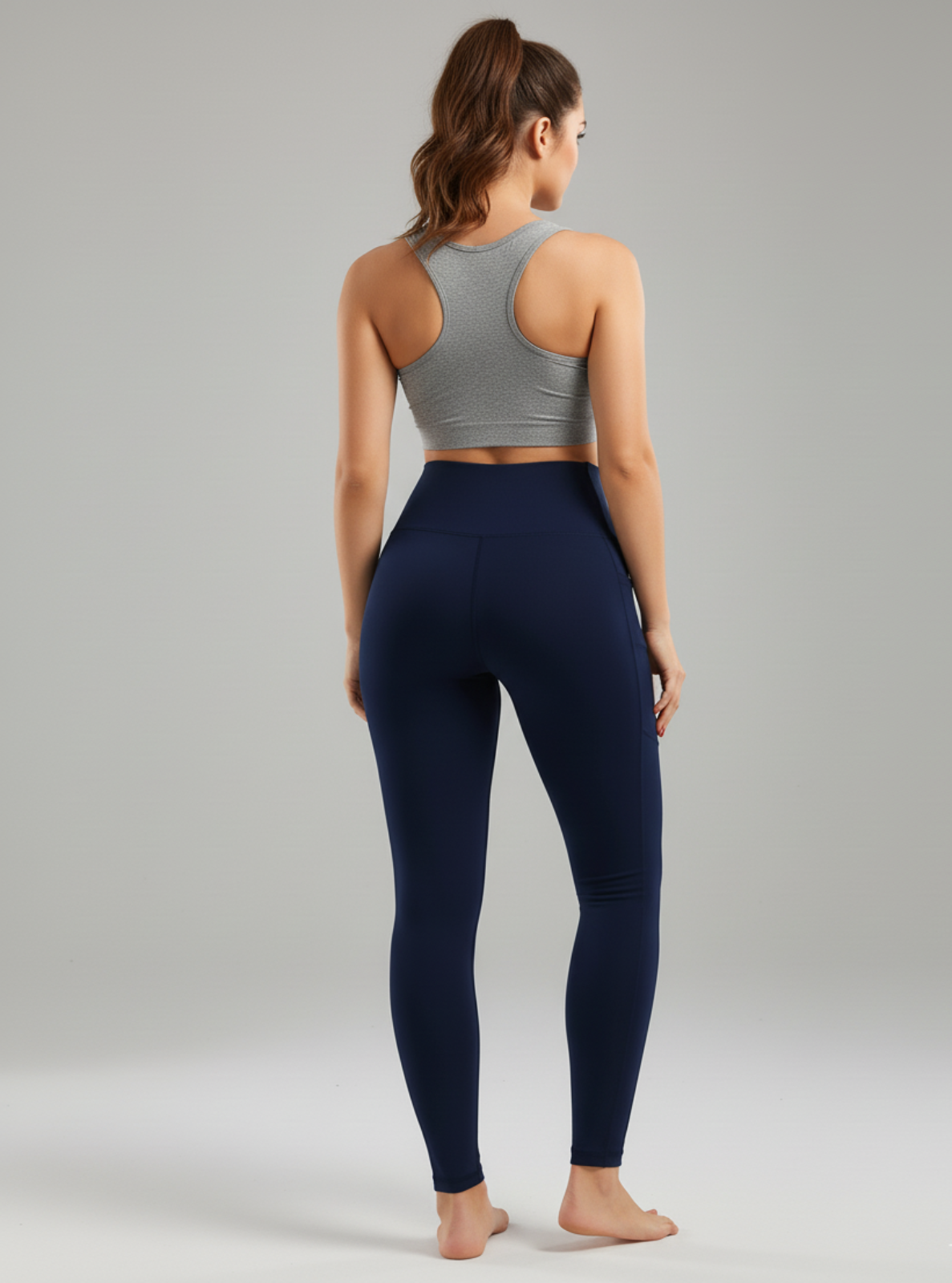 Woman wearing a gray sports bra and navy leggings on a plain background