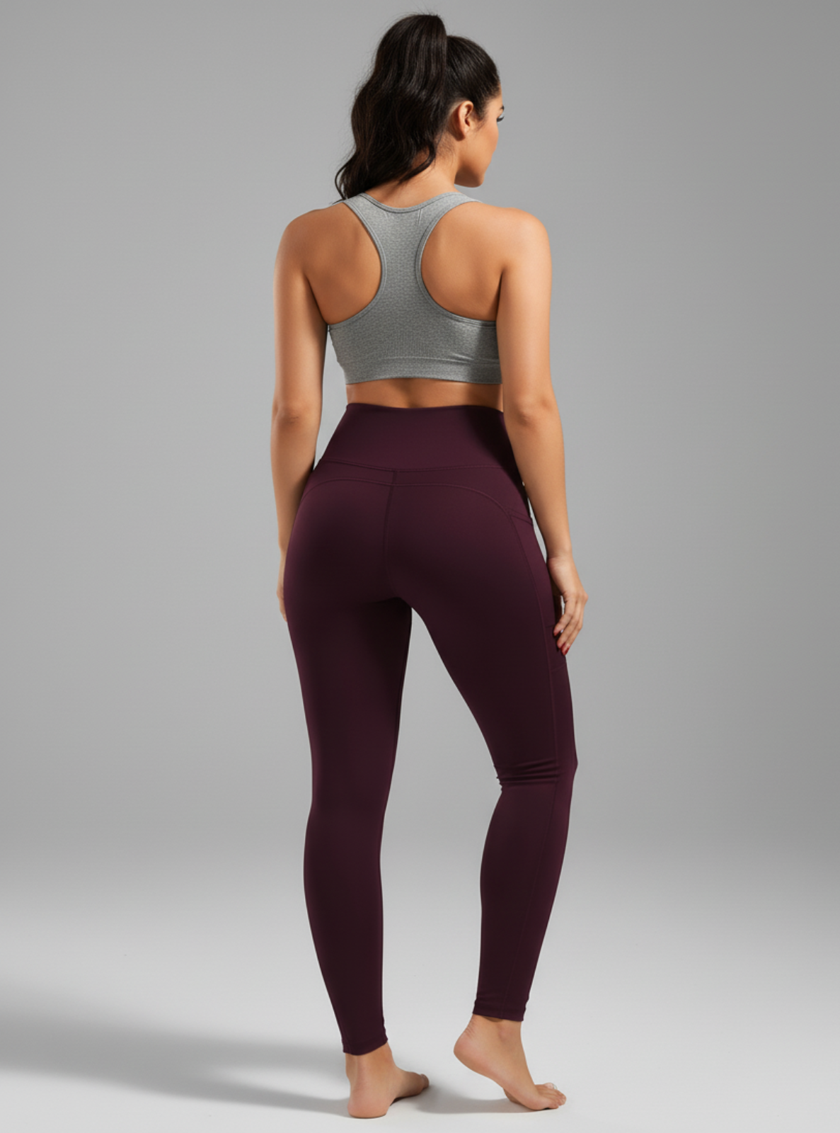 Woman wearing a gray sports bra and maroon leggings on a gray background